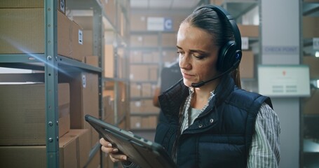 Female Logistics Coordinator Wearing Headset Uses Tablet Computer in Warehouse Facility. Sorting...