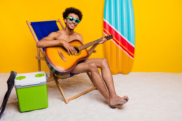 Young man enjoying summer vibes playing guitar at beach setting with vibrant yellow background.
