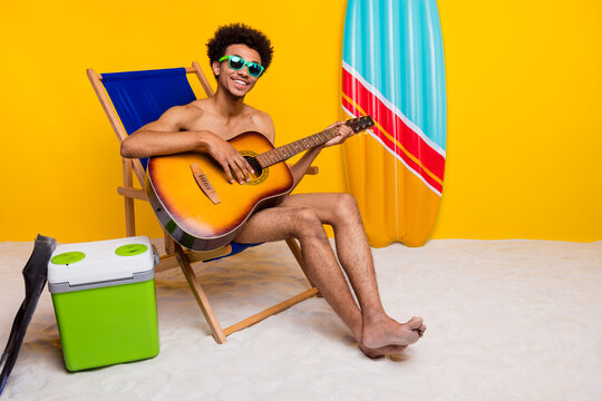 Young man enjoying summer vibes playing guitar at beach setting with vibrant yellow background.