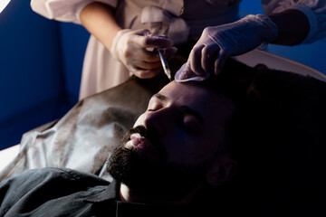 An attractive man receives mesotherapy injections to treat hair loss at the clinic. Injections into...