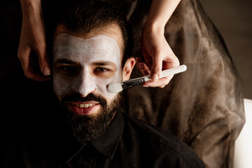 A beautician applies a scrub to the face of an older man in a spa, side light