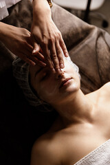 Close-up portrait of a beautiful woman receiving a facial massage with moisturizer in a beauty spa with side light. Natural cosmetics for skin care. Health care, beauty