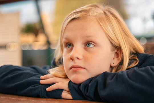 Close up portrait of pre-teen boy with long blond hair and blue eyes resting chin on hands looking