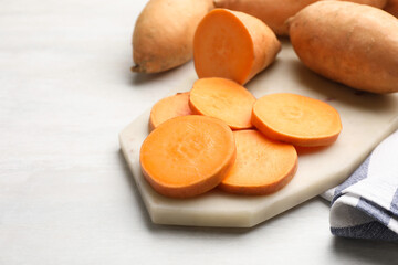 Fresh sweet potatoes and kitchen towel on white table, closeup. Space for text