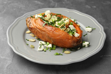Tasty cooked sweet potato with feta cheese, pumpkin seeds and green onion on grey table, closeup