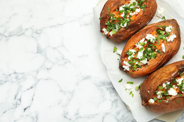 Tasty cooked sweet potatoes with feta cheese, green onion and parsley on white marble table, top view. Space for text