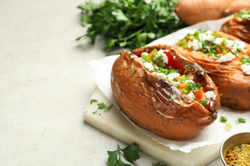 Tasty cooked sweet potatoes with feta cheese, green onion and parsley on gray textured table, closeup. Space for text