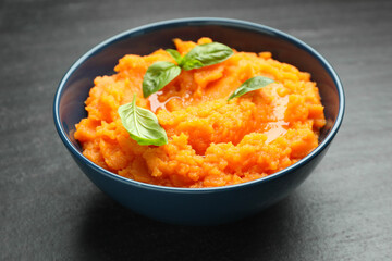 Tasty mashed sweet potato with basil in bowl on dark gray textured table, closeup