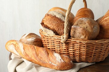 Different freshly baked bread loafs and wicker basket on wooden table, closeup