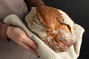 Woman with loaf of freshly baked bread on black background, closeup