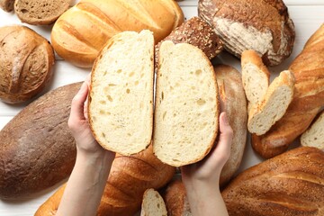 Woman with pieces of fresh bread over different other loafs at white table, top view