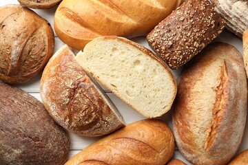 Whole and cut bread loafs on white wooden table, flat lay