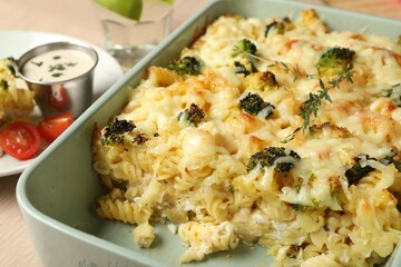 Tasty pasta casserole with cheese and broccoli in baking dish on wooden table, closeup