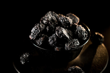 Dried prunes arranged beautifully on a dark plate showcasing rich textures against a black background