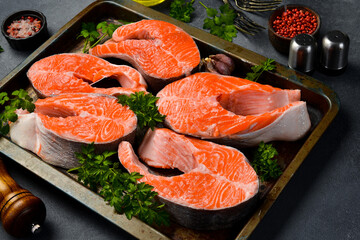 Set of fresh salmon or trout steaks with lemon, spices and parsley. Dark textured background.