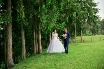 A bride and groom are walking through a forest, holding hands and carrying a bouquet. Scene is romantic and peaceful, as the couple enjoys their special day surrounded by nature