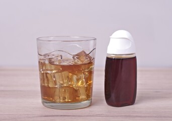 Drink with ice cubes next to s Syrup Concentrate bottle.