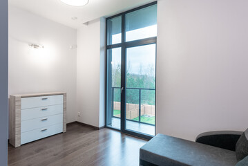 Obraz premium Modern bedroom with large window overlooking a tranquil landscape. A dresser and chaise lounge complete the serene atmosphere. Home Interior