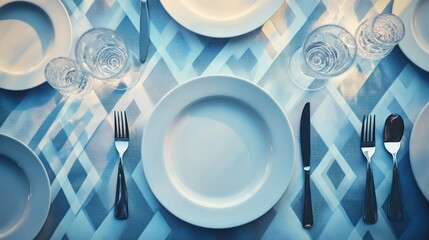 Overhead view of elegant table setting with white plates, silverware, and glasses on a blue patterned tablecloth.