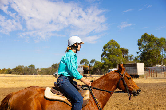 upper body view of teen girl riding chestnut horse on dry ground with blue cloudy sky and trees