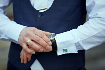 Obraz premium A man wearing a blue vest and white shirt is checking the time on his watch. The watch is black and has a gold band. The man's hands are on his watch, and he is in a hurry