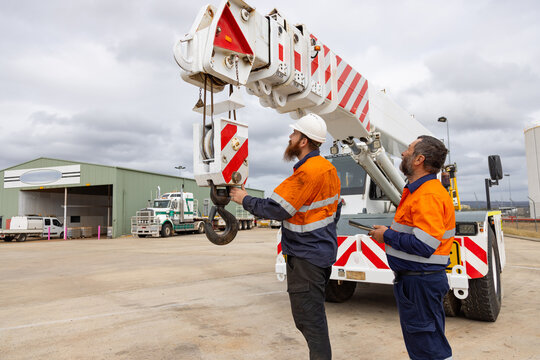 Two workers checking the parts of the crane truck on industrial site