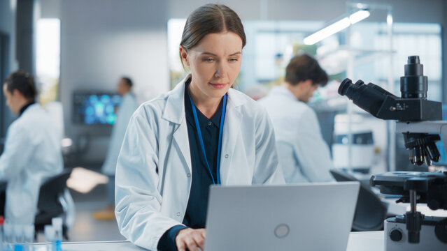 Caucasian Female Medical Research Scientist Work on a New Generation Medical Products in a Modern Laboratory. Young Woman Working on a Laptop Computer, Browsing Research Data Online