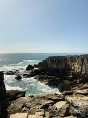Coastal view of rocky cliffs and ocean waves under a clear blue sky