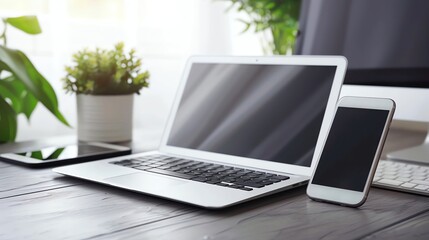 Fototapeta premium A laptop, tablet, and smartphone on a wooden desk in a bright room.