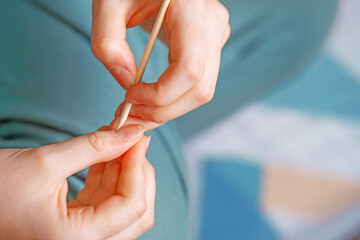 girl's hand gently cares for her nails using a wooden orange stick with a pointed tip, showcasing a...