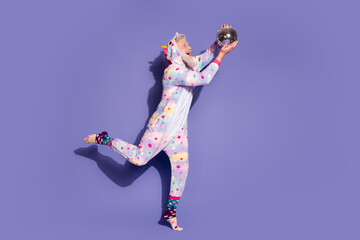 Cheerful man in a unicorn pajama poses with a disco ball on a vibrant purple background, embracing whimsical fashion