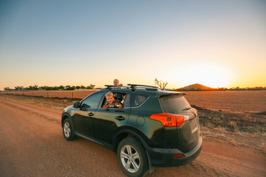 Little kids hanging out window and sunroof of small vehicle on dirt road
