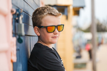 Boy in sunglasses leans on colourful beach wall, exuding a carefree, relaxed vibe