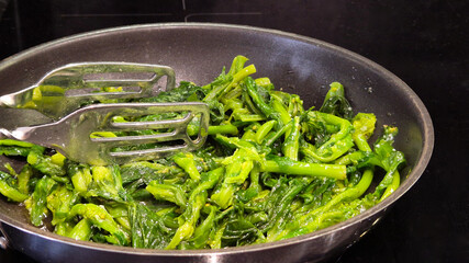 Fresh turnip greens sauteed in olive oil, garlic, and seasonings in a frying pan. A traditional and flavorful Portuguese side dish, served warm for a wholesome, healthy meal.