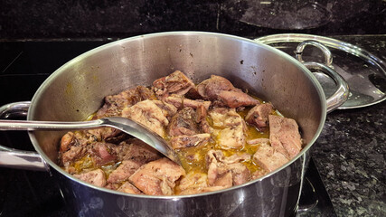 Turkey meat being stewed in a pot over an induction stove, with a spoon used to stir the dish. A hearty and flavorful meal prepared for a homemade family lunch or dinner.