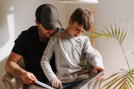 Father and son looking at an album while sitting on the couch.