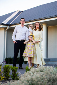 Portrait of family of four standing together outside home dad mum and two children