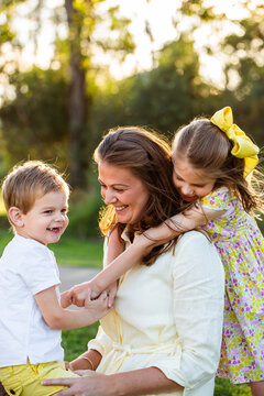 Happy mum with her two children daughter hugging her in golden evening light outdoors