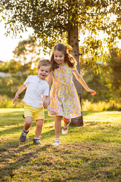 Brother and sister holding hands running together outside at park in golden yellow evening light