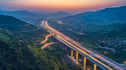 Obraz premium An overhead image of a freeway bridge that connects towns at nightfall, spanning a valley with green hills and forests, as part of infrastructural expansion. 