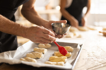 Baker's hands grease pieces of dough on baking sheet