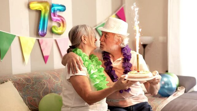 Elderly happy couple of grandparents at home celebrate grandfather&rsquo;s 75th birthday expressing affection and love
