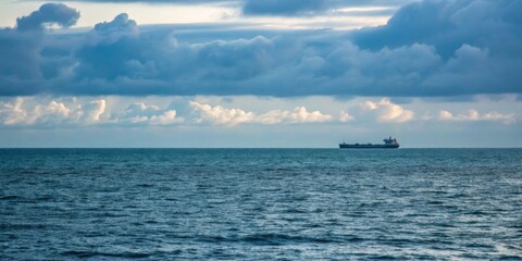 Obraz premium Calm ocean view with a distant cargo ship under a cloudy sky during twilight