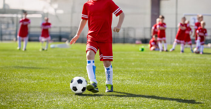 Young Soccer Players Running With Ball In Training Drill. Kids in Soccer Red Uniforms. Soccer Stadium in the Background. Football Soccer Players Running with Ball. Footballers Kicking Football Match.