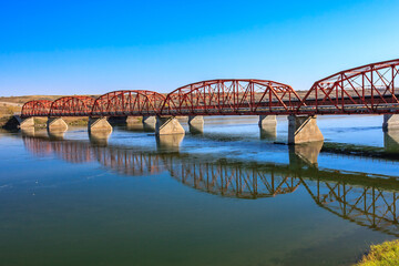 Fototapeta premium A red bridge spans a river, with the water reflecting the bridge's red color