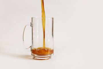 Pouring kvass into a mug on a light background, close-up. A glass of beer or kvass on a gray background. A traditional beer mug with a handle. Close-up of a glass being poured with a cool, tasty drink