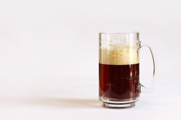 Kvass in a glass, light background. Glass of dark beer or kvass with foam in a glass on a light gray background. Traditional beer mug with a handle. Close-up on a glass with a cool tasty drink