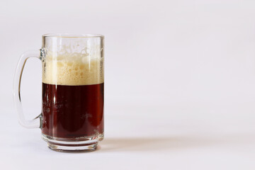 Kvass in a glass, light background. Glass of dark beer or kvass with foam in a glass on a light gray background. Traditional beer mug with a handle. Close-up on a glass with a cool tasty drink