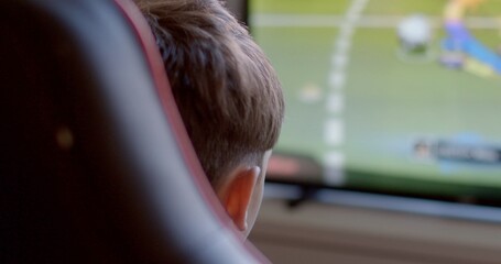 A child is deeply focused on their gaming console, enthusiastically playing an engaging soccer video game that involves competitive gameplay and requires strategy and skill development