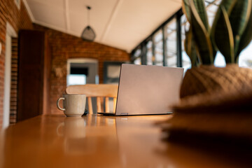 Cosy workspace with laptop, coffee, and plant on a sunny wooden table with brick walls